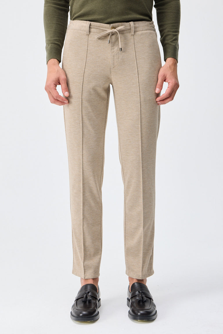 Herenbroek met trekkoord in taupe- of havermoutbeige kleur, getailleerde pasvorm en taps toelopende pasvorm.
