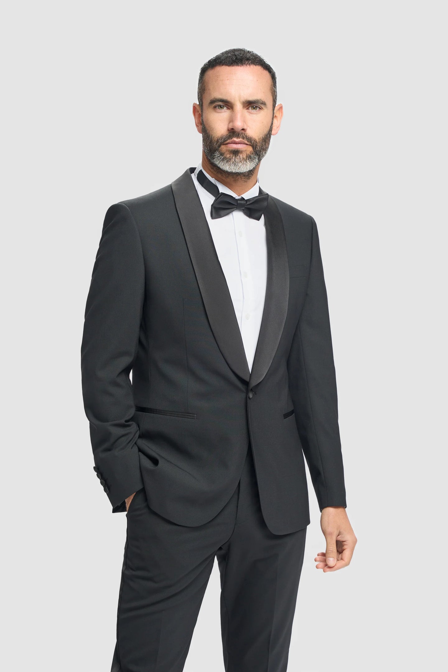 Man wearing a black tuxedo with a white shirt and black bow tie on a light gray background