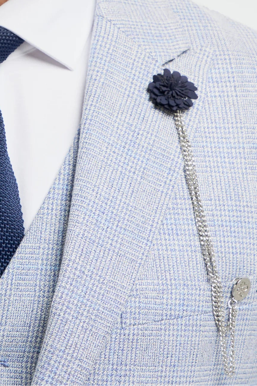 Man in een lichtgrijs pak met een donkerblauwe stropdas en bloemspeld op een witte achtergrond.